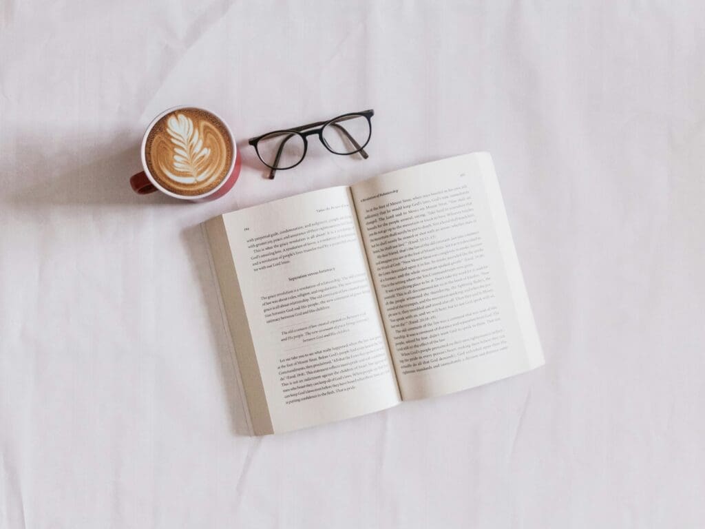 an open book next to a pair of glasses and a latte